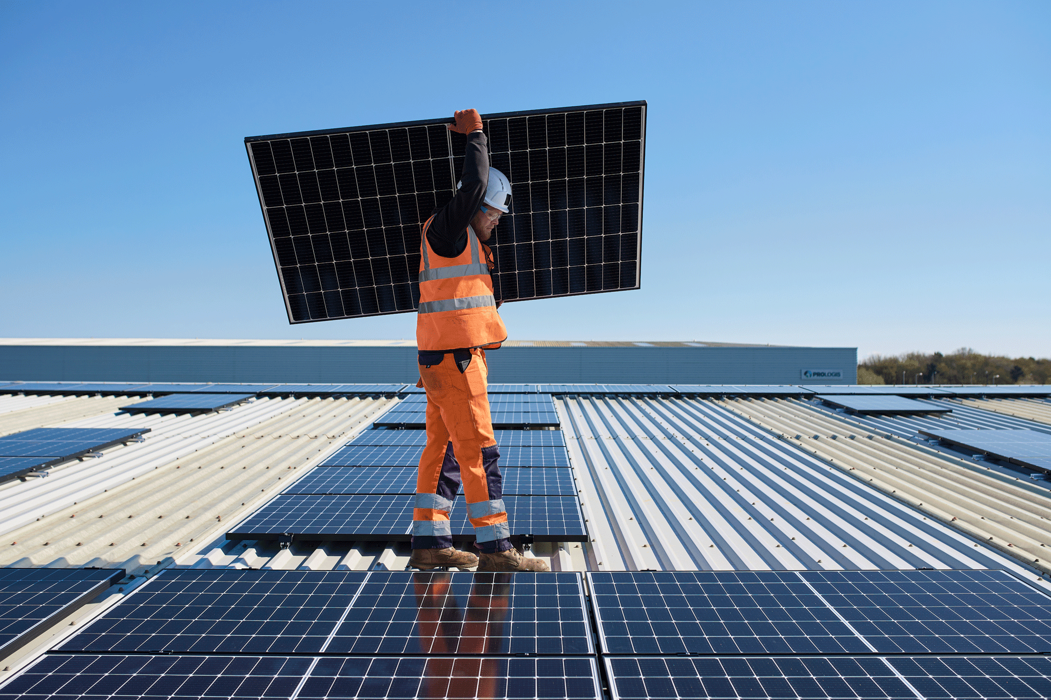 Una persona transportando un panel solar sobre un tejado